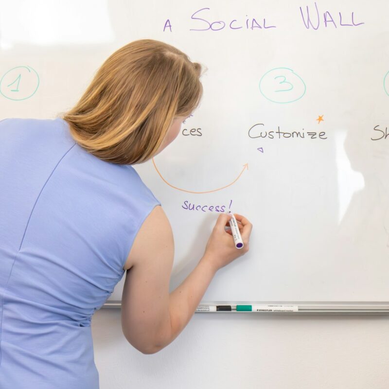 a woman writing on a white board with marker