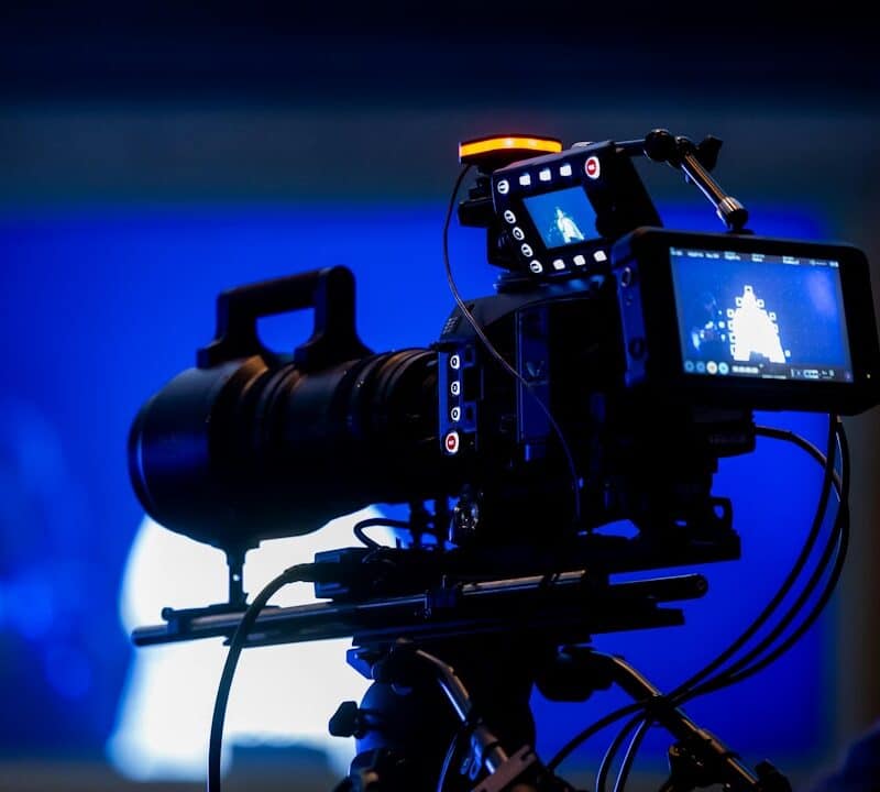 Professional video camera on tripod with blue background