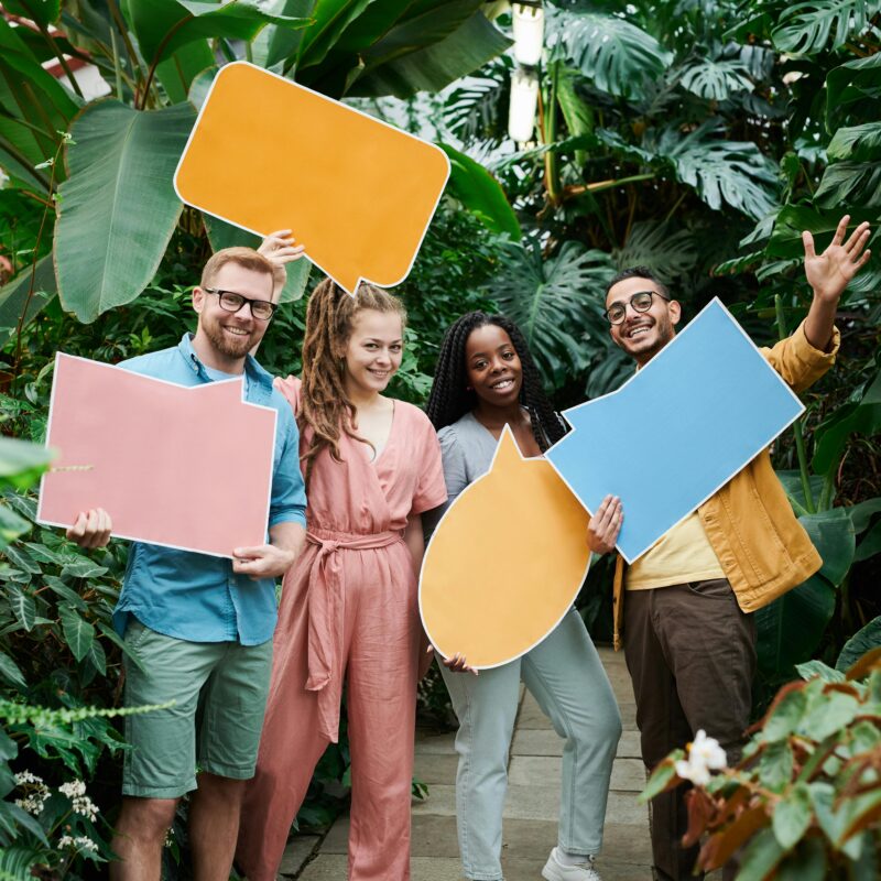 Four people standing in front of foliage holding blank speech bubble poster boards