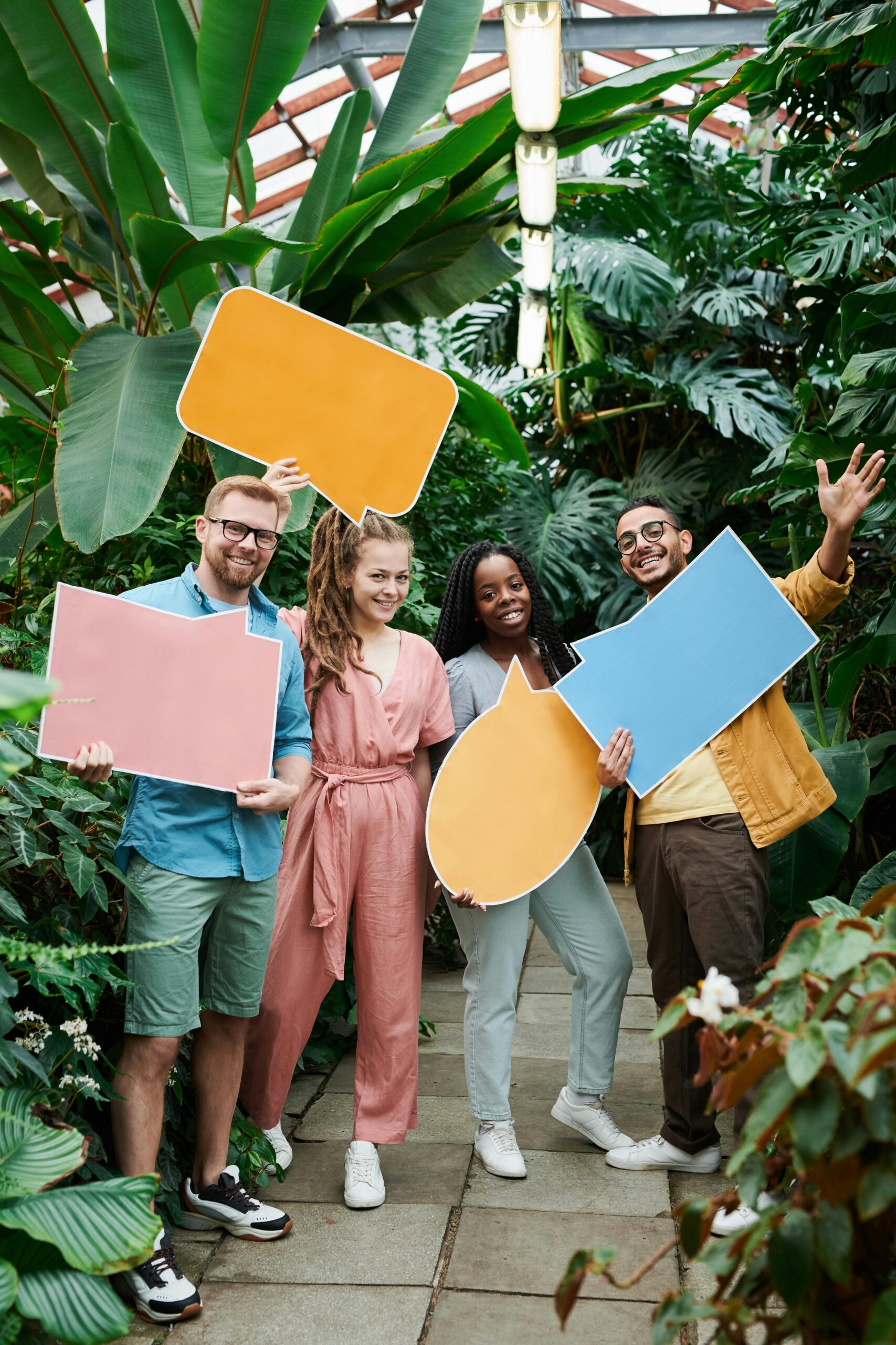 Four people standing in front of foliage holding blank speech bubble poster boards