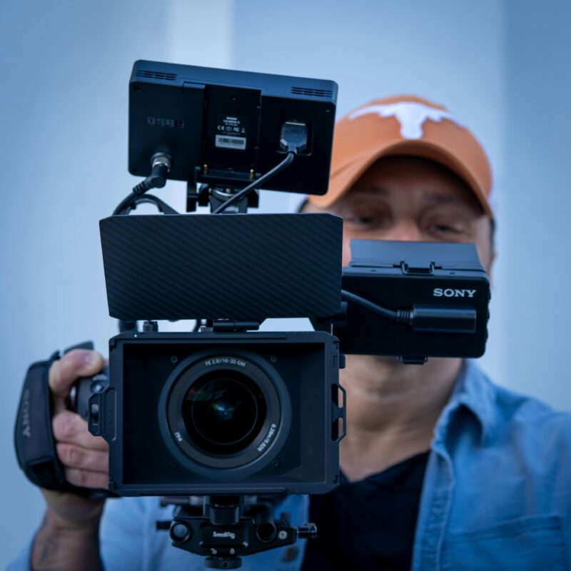 A man in an orange Texas Longhorns ball cap holding a professional video camera