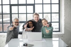 Two men and two women sitting in front of a laptop and posing with their thumbs up