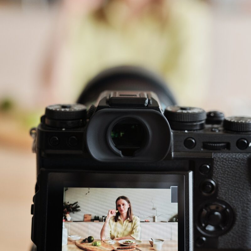 A woman in the background blurred out with the focus on the production camera filming her