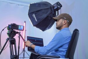 Man in a blue shirt and ball cap monitoring a recording of a professional camera
