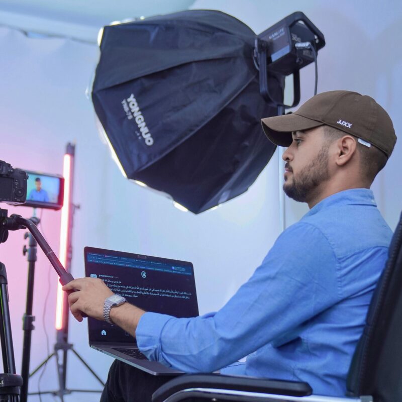 Man in a blue shirt and ball cap monitoring a recording of a professional camera