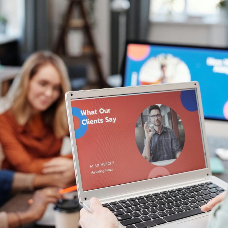 Focus on a laptop with a slide up that says "What Our Clients Say" with a woman in the background