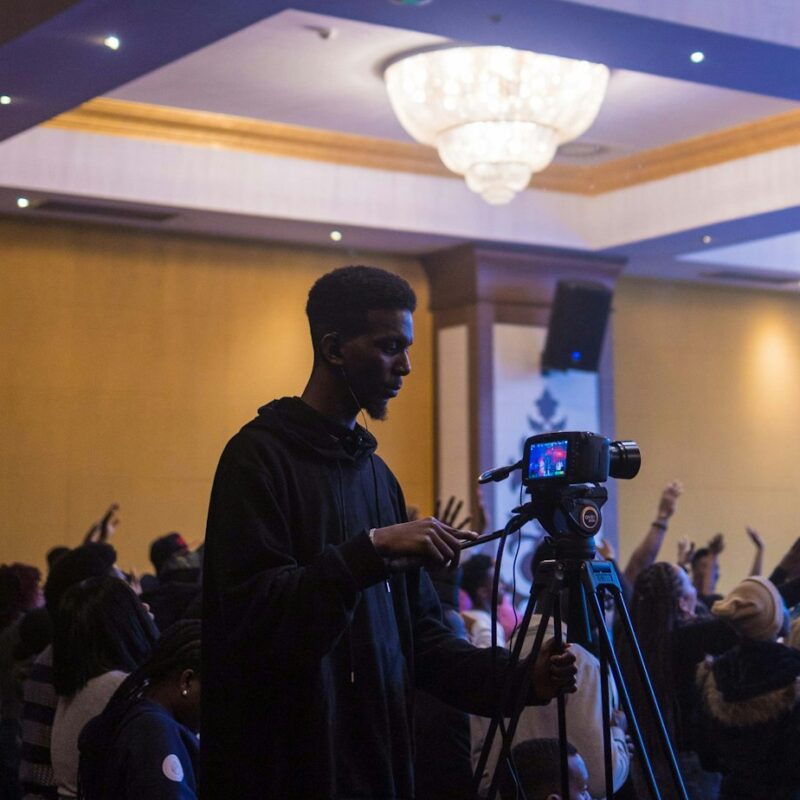 a man standing next to a camera in front of a crowd of people