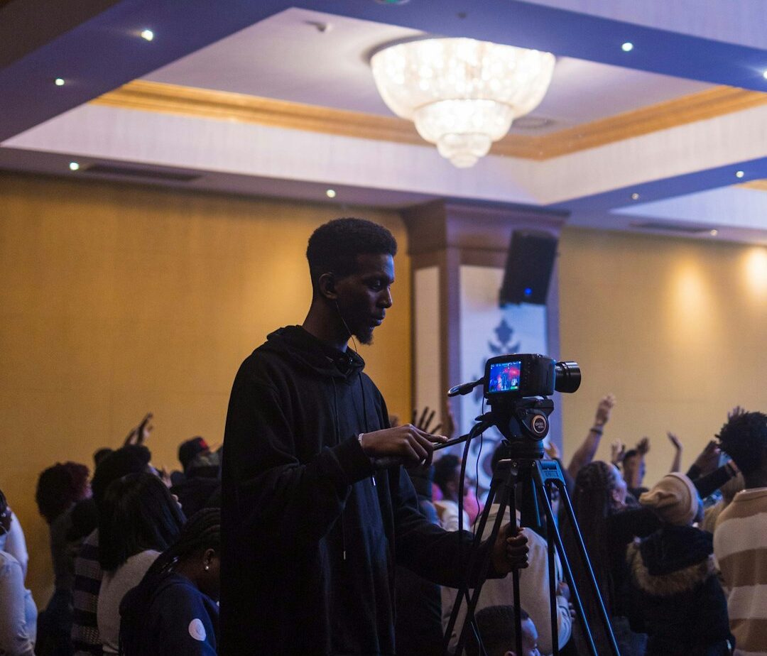 a man standing next to a camera in front of a crowd of people